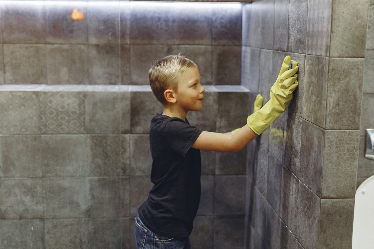 A boy cleans shower walls and time management experts encourage parents to get children to help with the house