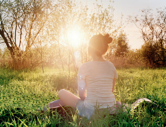 Young woman is sitting in yoga position and enjoying the sunset in nature