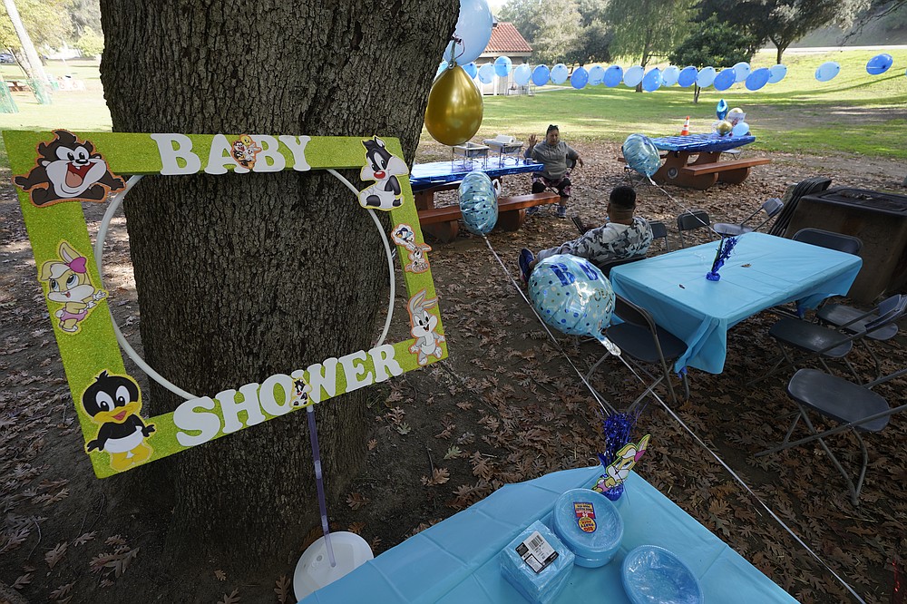 Estela Ortiz and her son Julio Boror hold tables for their guests celebrating an outdoors baby shower party in Elysian Park Los Angeles, Saturday, Nov. 6, 2021. A vaccine mandate that is among the strictest in the country takes effect Monday, Nov. 8, in Los Angeles, requiring proof of shots for everyone entering a wide variety of businesses from restaurants to shopping malls and theaters to nail and hair salons. (AP Photo/Damian Dovarganes)
